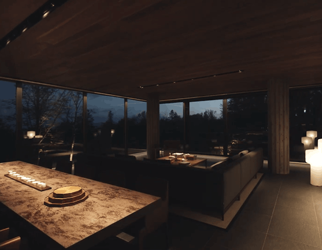 modern-dim-living-room A dimly lit, modern open-plan living and dining room with floor-to-ceiling windows overlooking a forest.